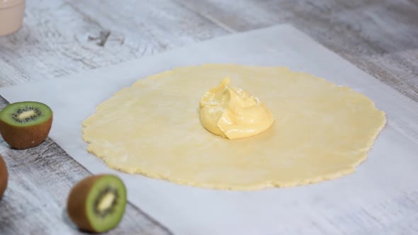 Female hands put cream on the raw dough. Making galette with fresh kiwi