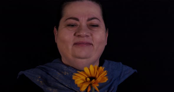 Elder woman looking into the camera holding a dandelion