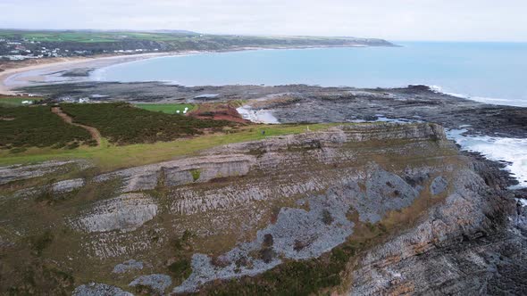 AERIAL: Pan out revealing rocky coastline and curved beach, Port Eynon, Gower, 4k Drone