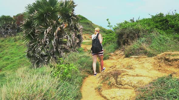 girl tourist with a backpack walking along a tropical island overlooking the sea