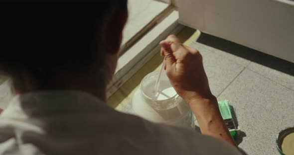 Close Up of Young Woman Mixing the Paint in a Glass Jar with His Hand Sunny Day