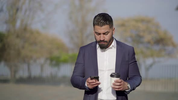 Man Holding Coffee To Go and Using Cell Phone Outdoor