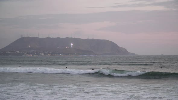 Sunset over surfers and seashore on Miraflores, Lima, Perú. Lighting cross in the background.