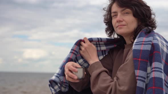 Woman Drinks Hot Tea From a Thermos While Sitting on the Beach