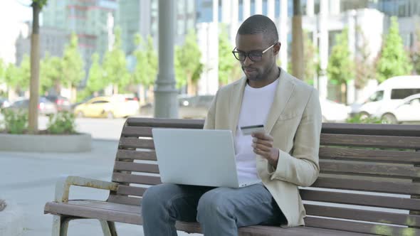 African Man Having Online Payment Failure on Laptop Sitting Outdoor on Bench