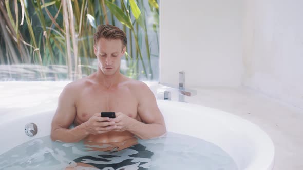 Young Man Reads Messages on Smartphone in Modern Bathtub