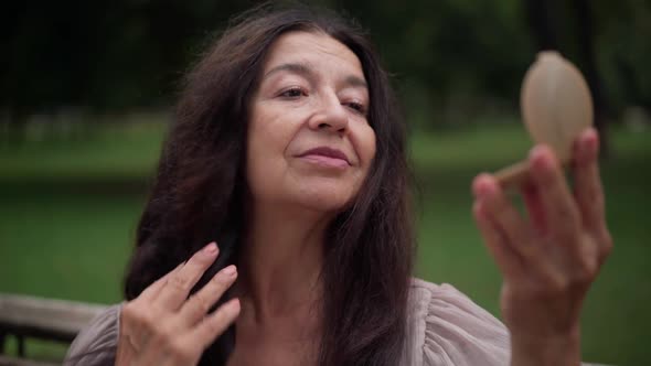 Closeup Portrait Beautiful Senior Woman with Long Black Hair Sitting in Park Admiring Reflection in