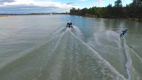 Aerial shot of young man wake boarding behind a motorboat in a lake.