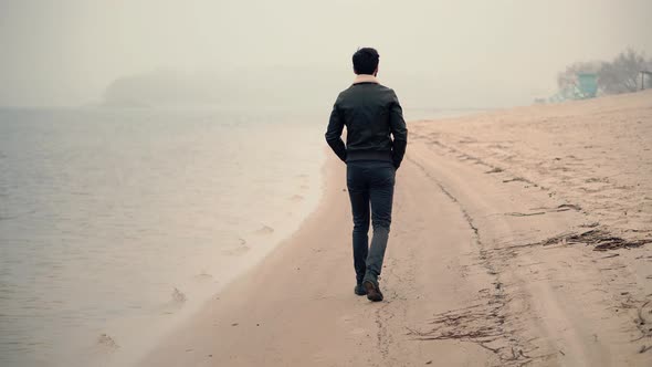 Man Walking On City Beach In Foggy Day. Guy In Sunglasses Walks On Sand.  Man Walking On Sand Beach.