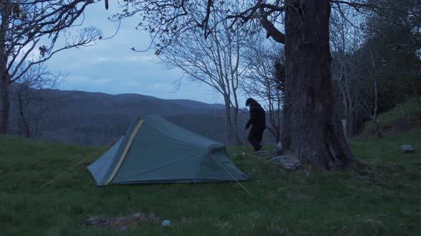 Young man camping carries rocks for outdoor fire WIDE