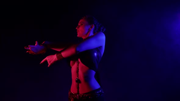 An Attractive Woman Is Dancing an Oriental Dance on a Black Smoky Background in the Studio Making