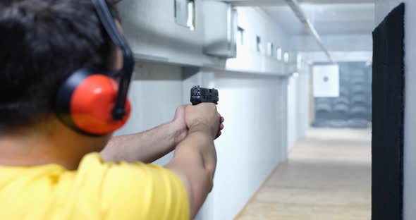 Rear View of Man Aiming Gun at Target in Shooting Range