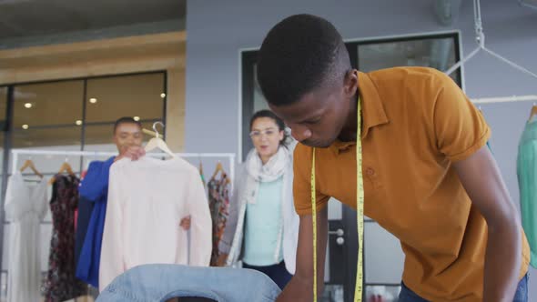 Three happy diverse male and female fashion designers standing in discussion, inspecting clothes