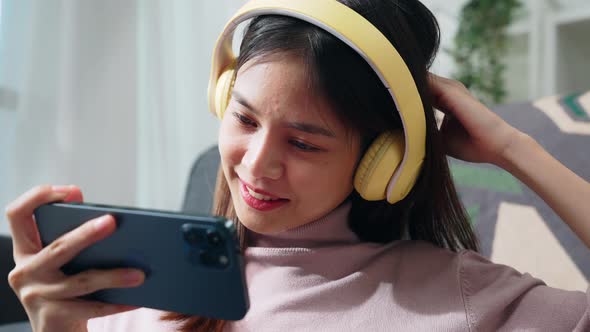 Woman sitting on sofa with holding the smartphone to watch movies on mobile application.