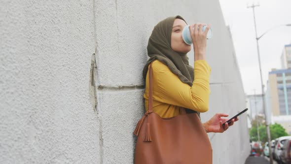 Woman wearing hijab drinking in the street with a take away coffee