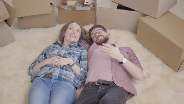 Cheerful Young People Discuss the Interior Layout of the Apartment Lying on a Fluffy Carpet