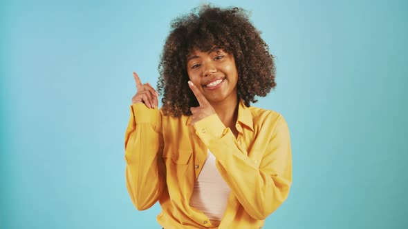 Africanamerican Young Female Pointing Up By Her Forefingers Asking you to Look Smiling Posing on