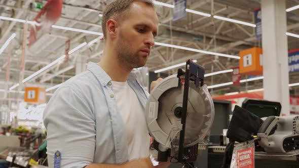 Man Chooses a Circular Saw in a Tool Shop