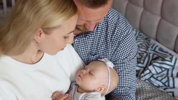 Mother and Father Hugging and Admiring Their Baby While the Child Sleeps in the Arms of the Mother