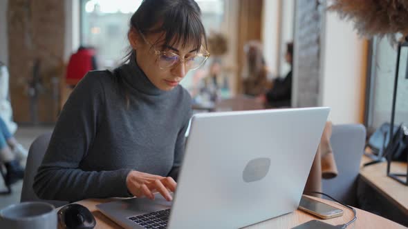 Portrait Young Woman in Eyeglasses Using Laptop in Coworking Space or Cafe and Smiling To Camera