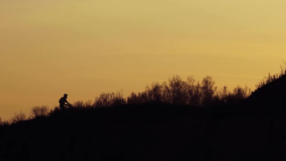 Silhouette of Motorcyclist Is Riding Off Road on Mountains at Sunset in Dark.