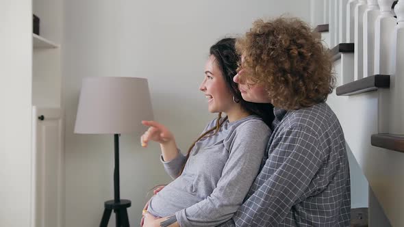 Pregnant Couple which Standing Near the Big Window and Gently Stroking Her Belly