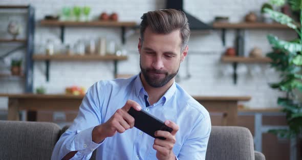 Male Millennial Professional Guy Holding Smartphone Playing Mobile Game