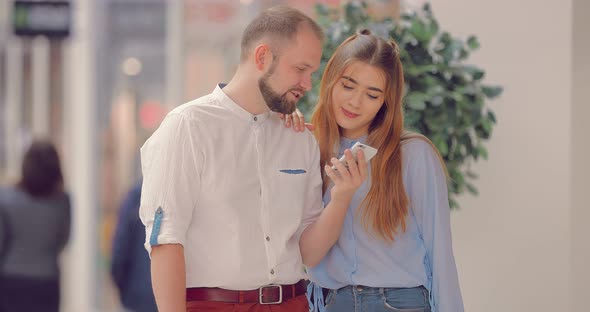 Couple in the Mall Looks at the Phone Screen and Talking About Something