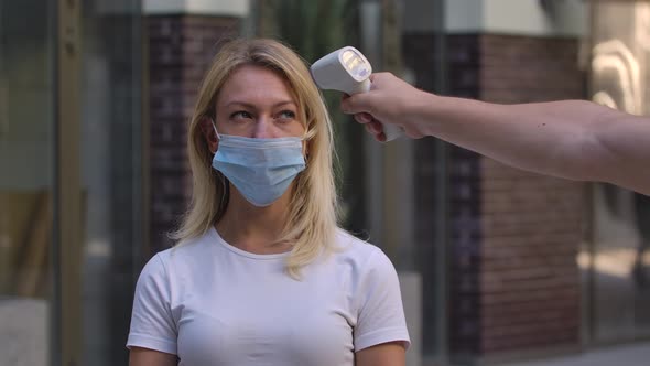 Portrait of Pretty Young Woman in Medical Mask Which the Temperature Is Measured with a Non Contact