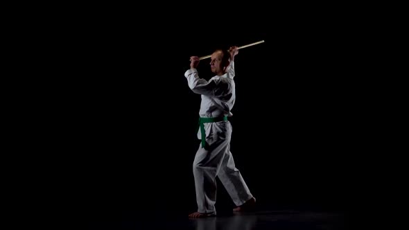 Kendo Fighter on White Kimono Practicing Martial Art with the Bamboo Bokken on Black Background