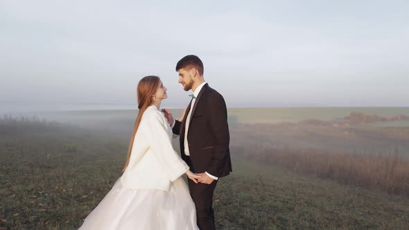 Newlyweds. Caucasian Groom with Bride on the Morning Field. Fog. Wedding Couple