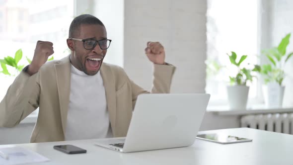 African Man Celebrating Success While Using Laptop in Office