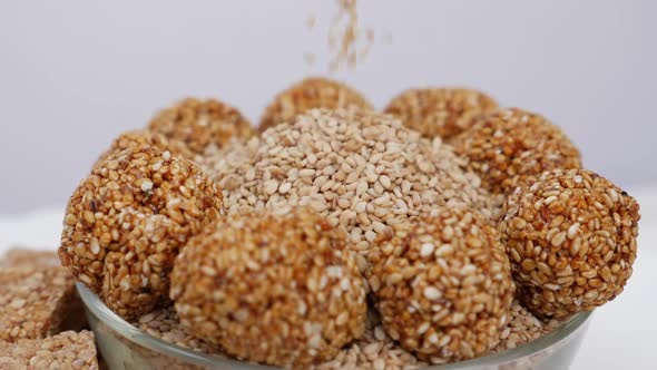 Rotating view of dropping sesame seeds over sesame ladoos filled in a bowl