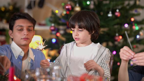 Middle Eastern Boy with Christmas Sparkler Sitting with Teenage Brother at Dinner Table Enjoying