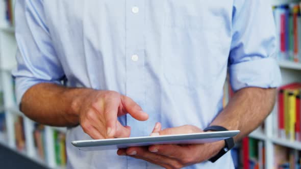 Mid-section of school teacher using digital tablet in library at school