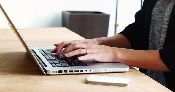 Mid section of female executive sitting at desk and using laptop