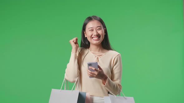 Woman With Shopping Bags Being Happy Be Able To Using Mobile Phone Shopping Online At Green Screen