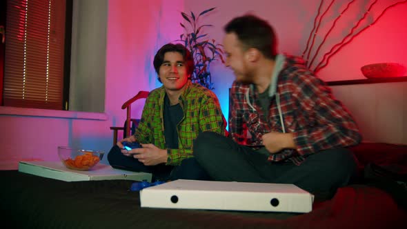 Young Man Sitting on the Bed and Playing Video Game - His Friend Comes To Him and Starting To