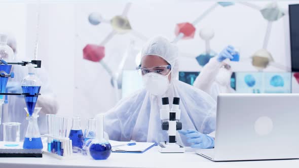 Woman Scientist Looking Through Microscope in Laboratory Wearing Protection Equipment alt