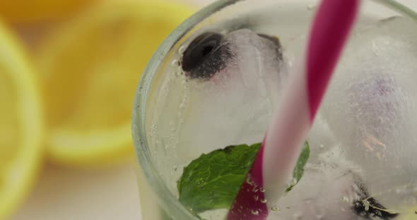 Stir of Cold Drink with Lemon, Mint Leaf, Ice Cubes and Black Currant in a Glass