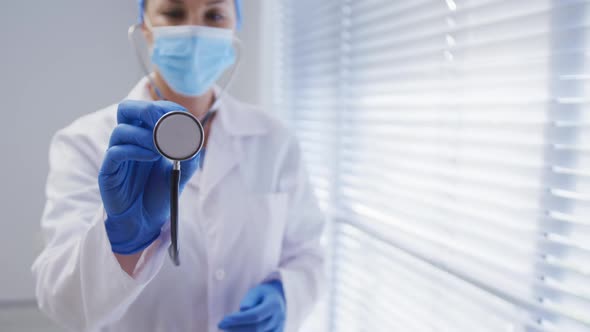 Caucasian female doctor wearing face mask and surgical gloves using stethoscope