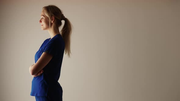 Goodlooking Caucasian Nurse in the Blue Suit Standing Sideways Medium Shot Studio Shot Beige