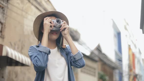 Happy woman young Asian traveler wearing retro fedora hat using film camera taking a photo.