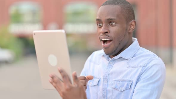 Outdoor Portrait of Excited African Man Celebrating Success on Tablet