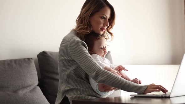 Young mother with a child on hands working with computer at home.