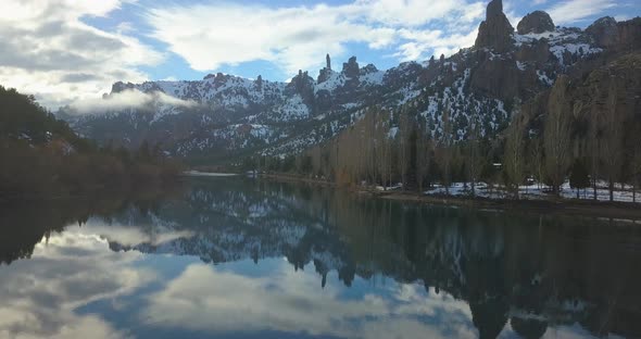 The cameraes slowly over a mirrored river surrounded by rocky mountains with the sun going down.