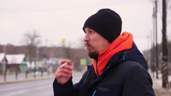A Man Smokes on the Side of the Road Looking at the Road with Cars