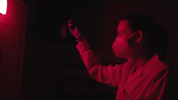 Woman Wearing Mask Looking At Laboratory Sample Through Infrared Light By Laboratory Tweezers.