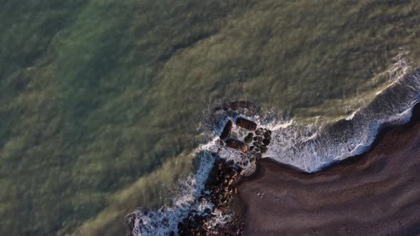 Slow rotation zoom, from a drone looking down on a man made rockpool on the beach.