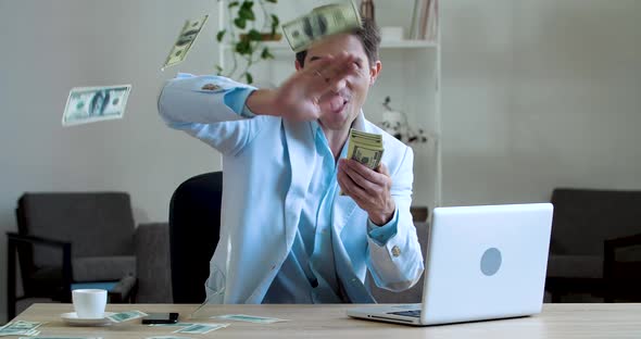 Young Happy Businessman Scatter Dollars Banknote and Make Winner Movement Sitting in Office. Money